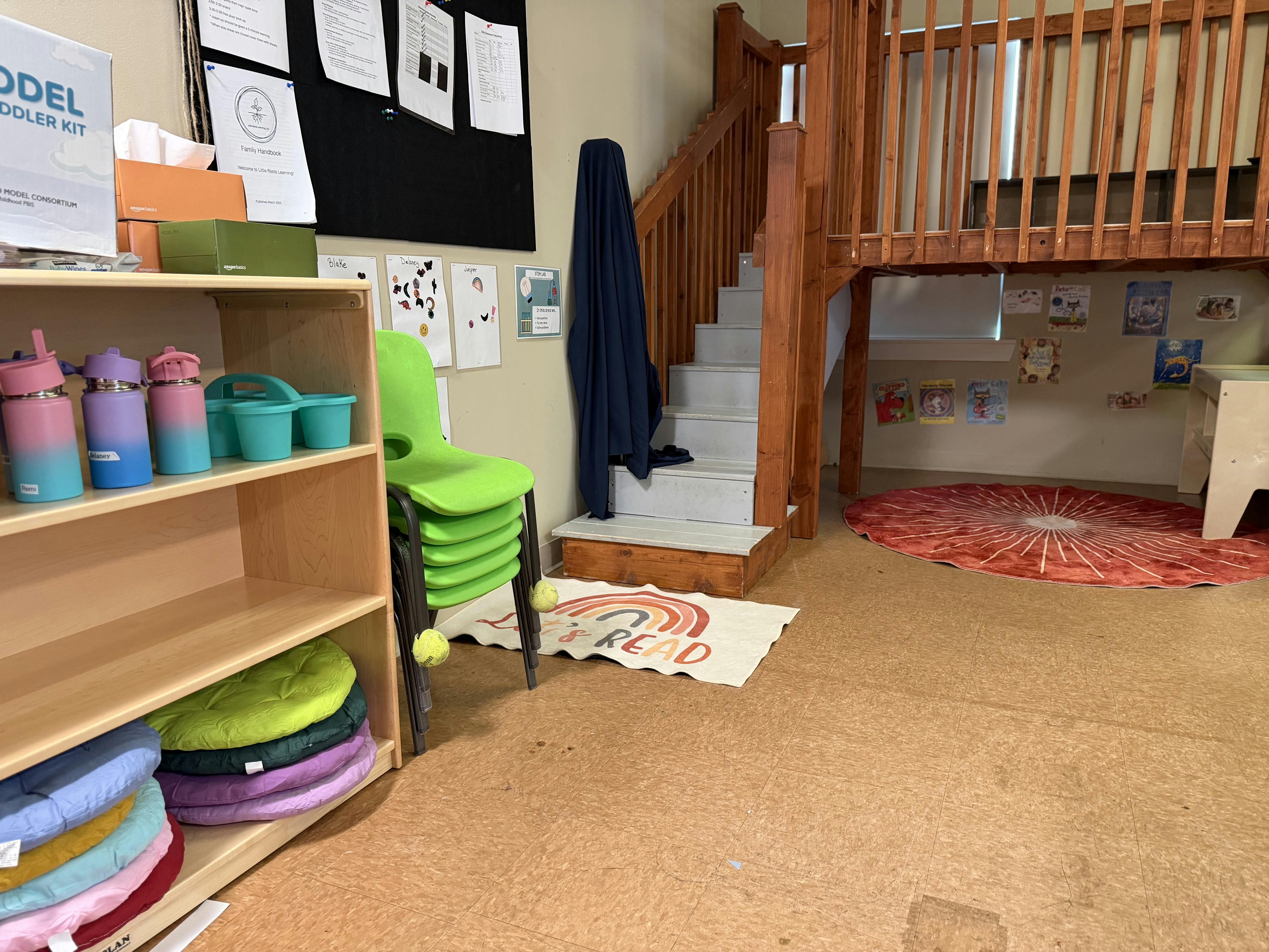 Classroom with a wooden play loft, cubbies, stacked chairs, and bulletin board