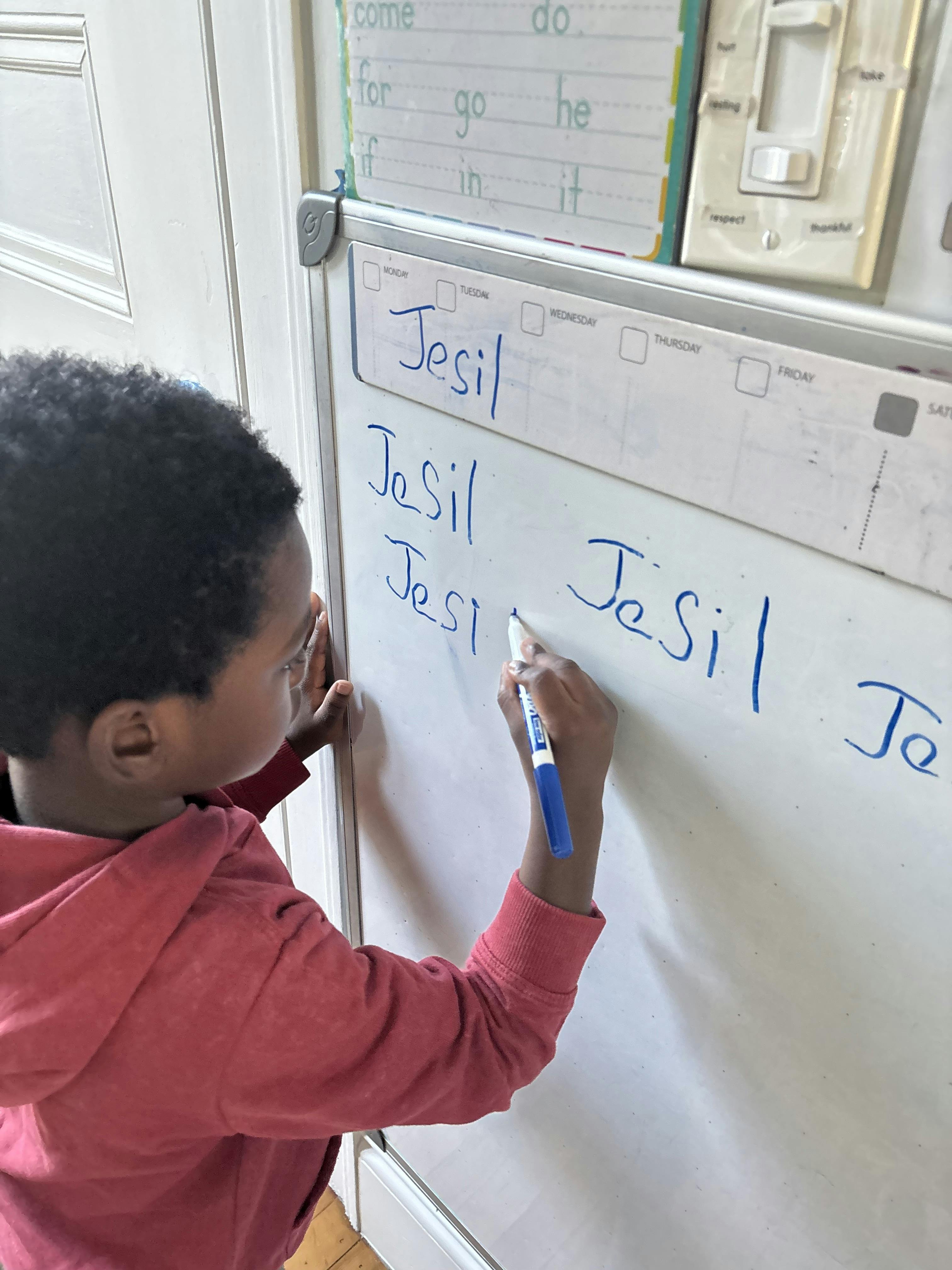 Child writing "Jesil" on a whiteboard