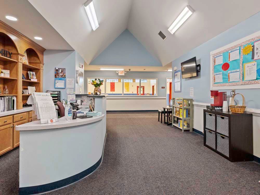 Reception area with a light blue curved desk, wooden shelving, and bulletin board