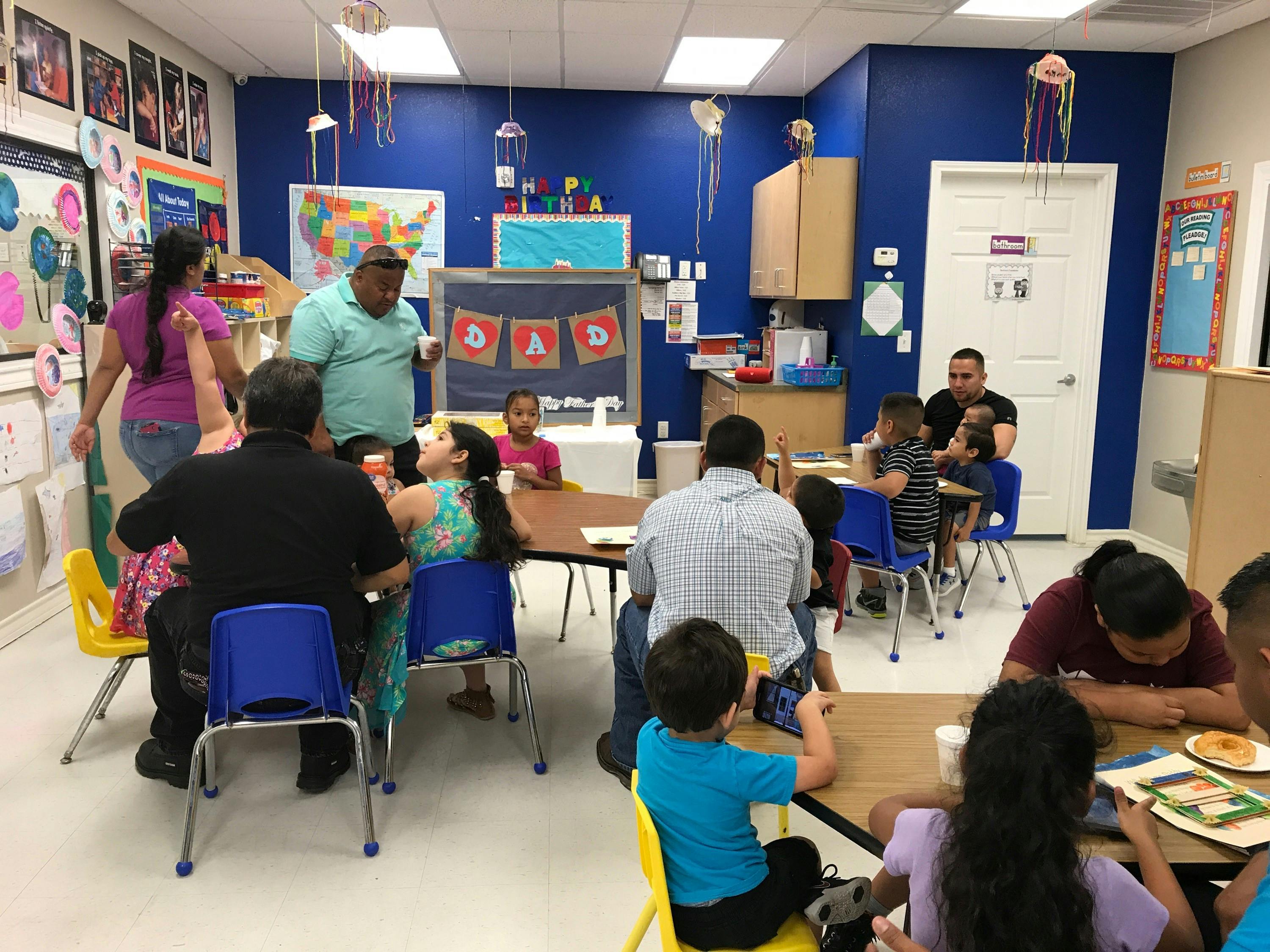 Adults and children gathered around tables in a classroom