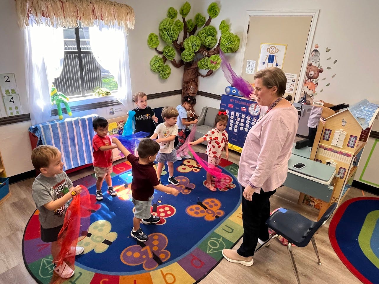 Adult and children dancing with colorful scarves in a classroom