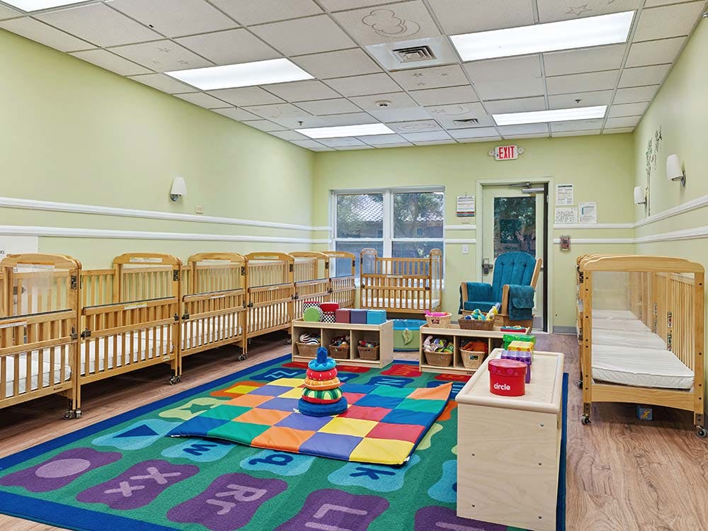 A room with multiple cribs lining the walls and a colorful rug on the floor