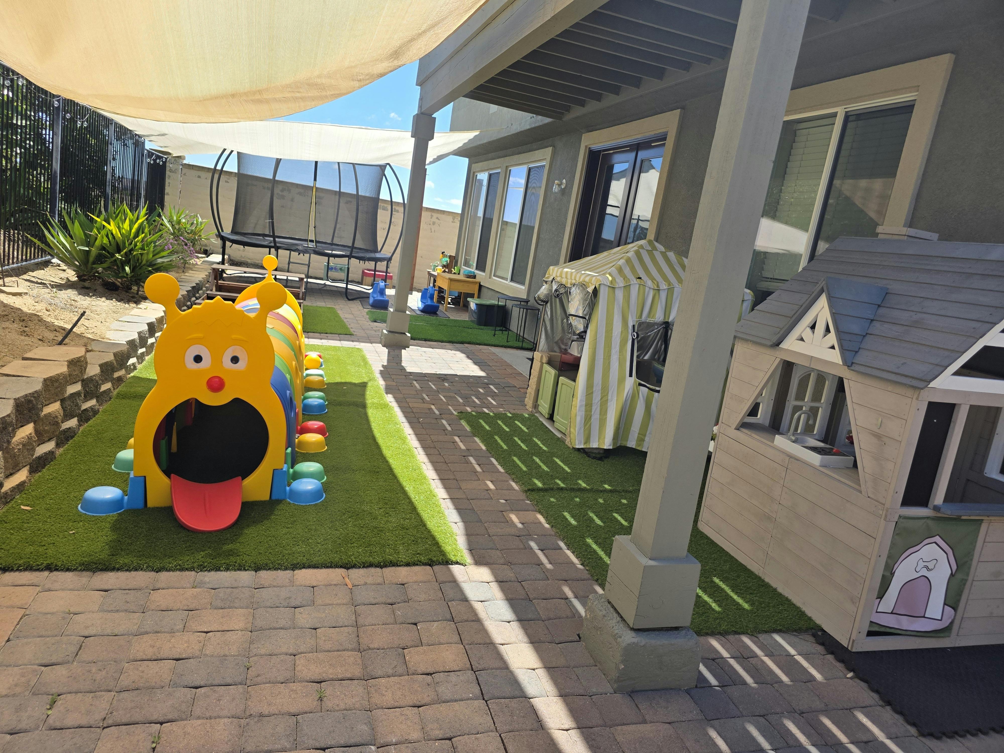 Play yard with a yellow caterpillar tunnel, trampoline, and playhouses
