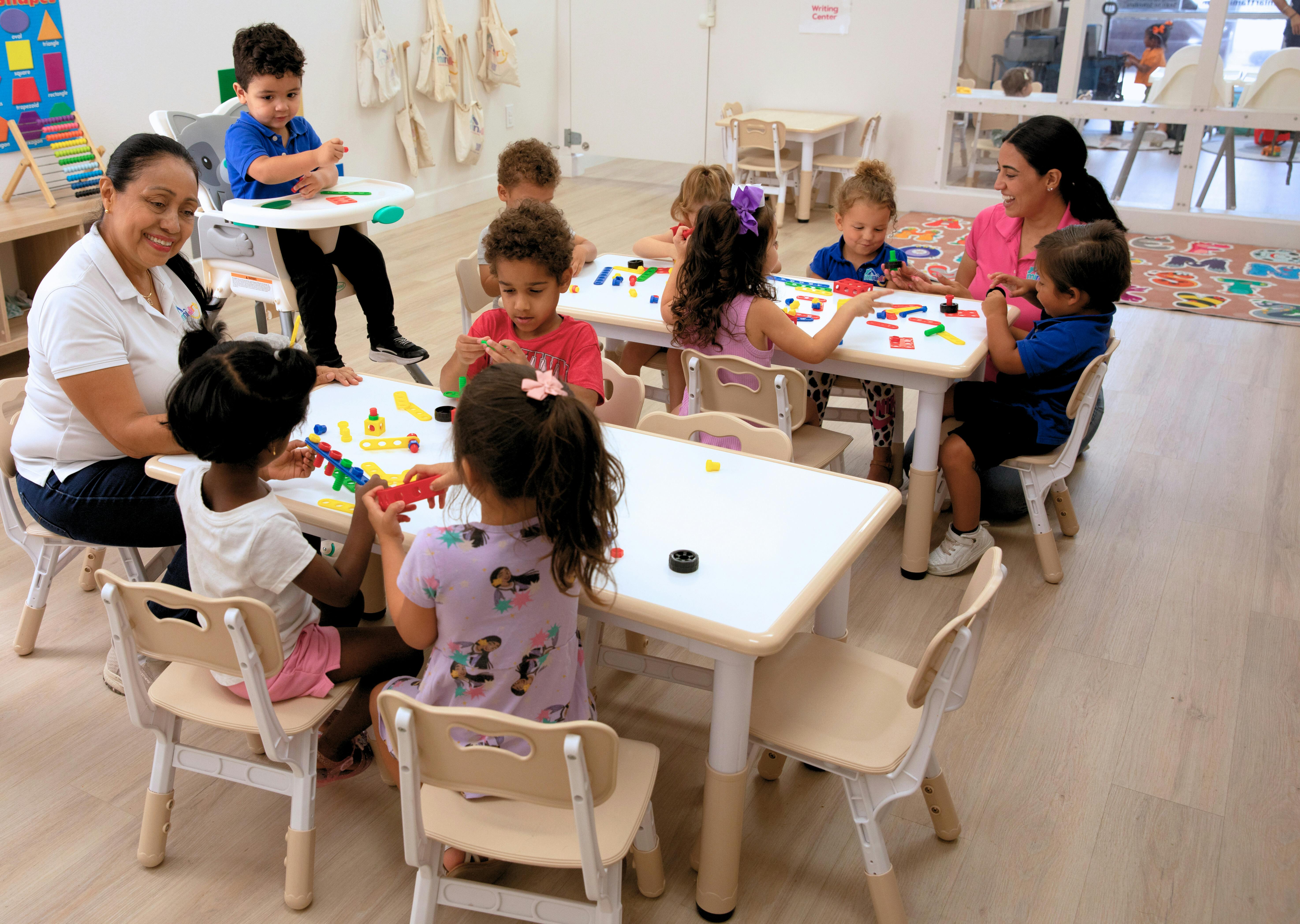 Two women supervising a group of children playing with building toys at tables