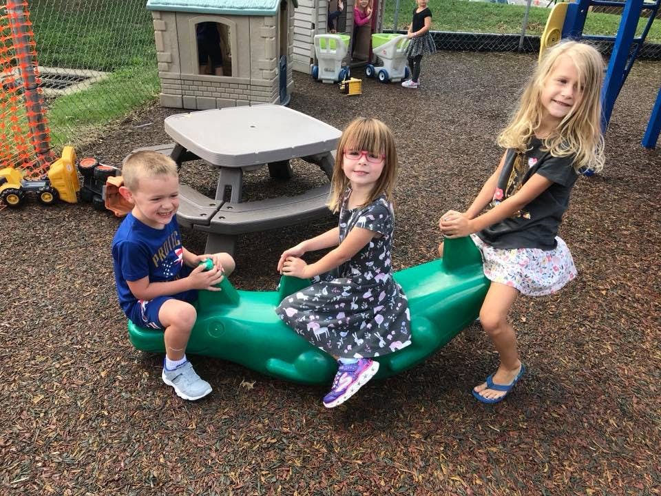 Three children playing on a green seesaw in a playground