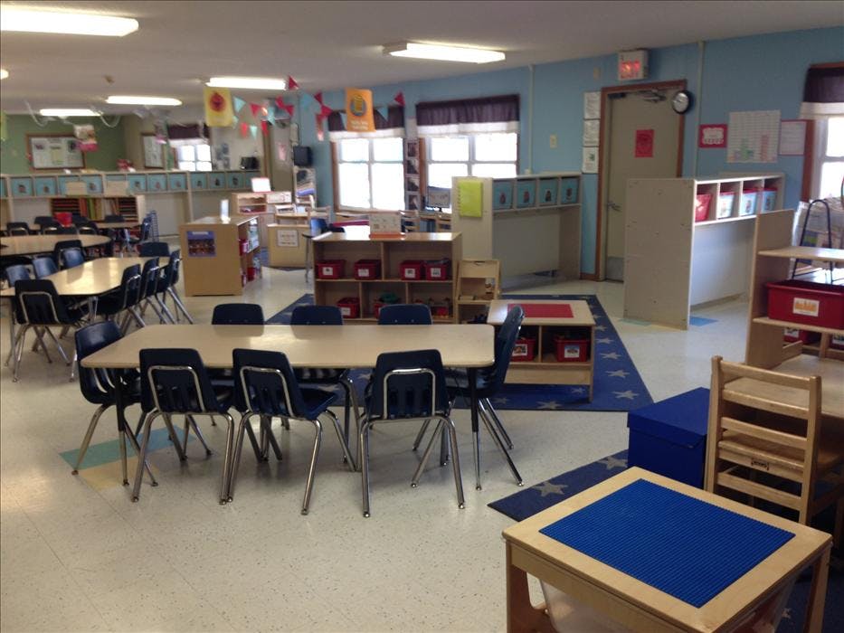Empty classroom with multiple tables and chairs, shelves, and play areas
