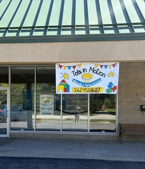 Tots in Motion business banner displayed on a glass storefront