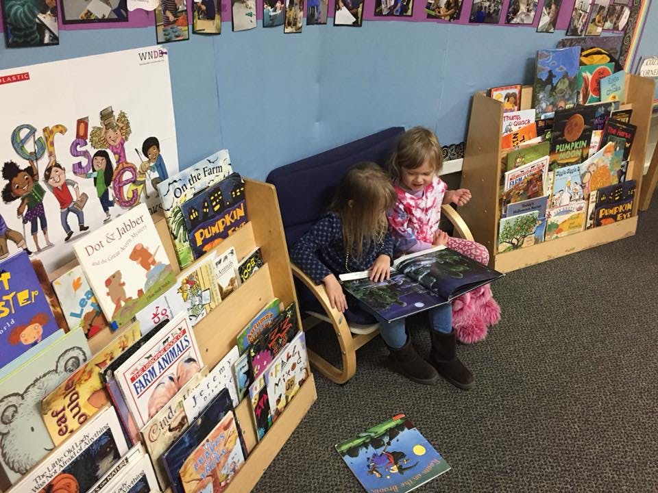 Two children sitting in a chair reading a book in a classroom