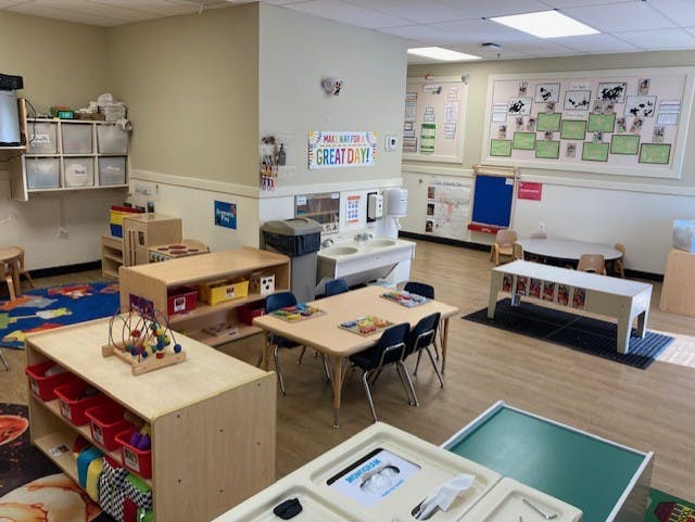 Classroom with child-sized tables, chairs, storage units, and a sink