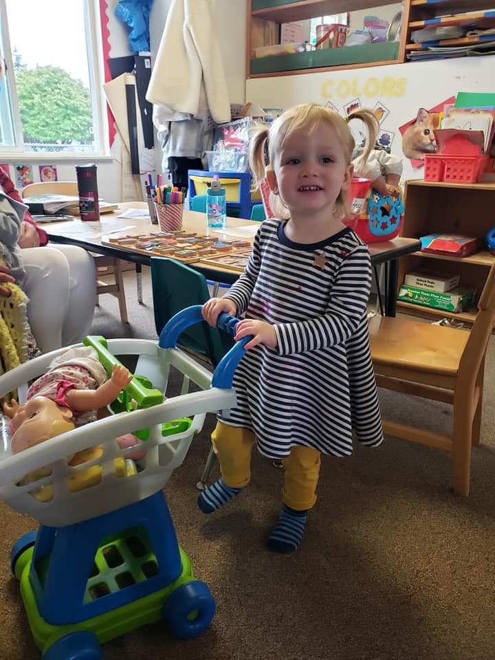 Child pushing a toy shopping cart with a doll in a classroom