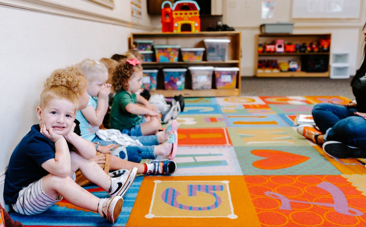 Children sitting on a colorful mat in a classroom