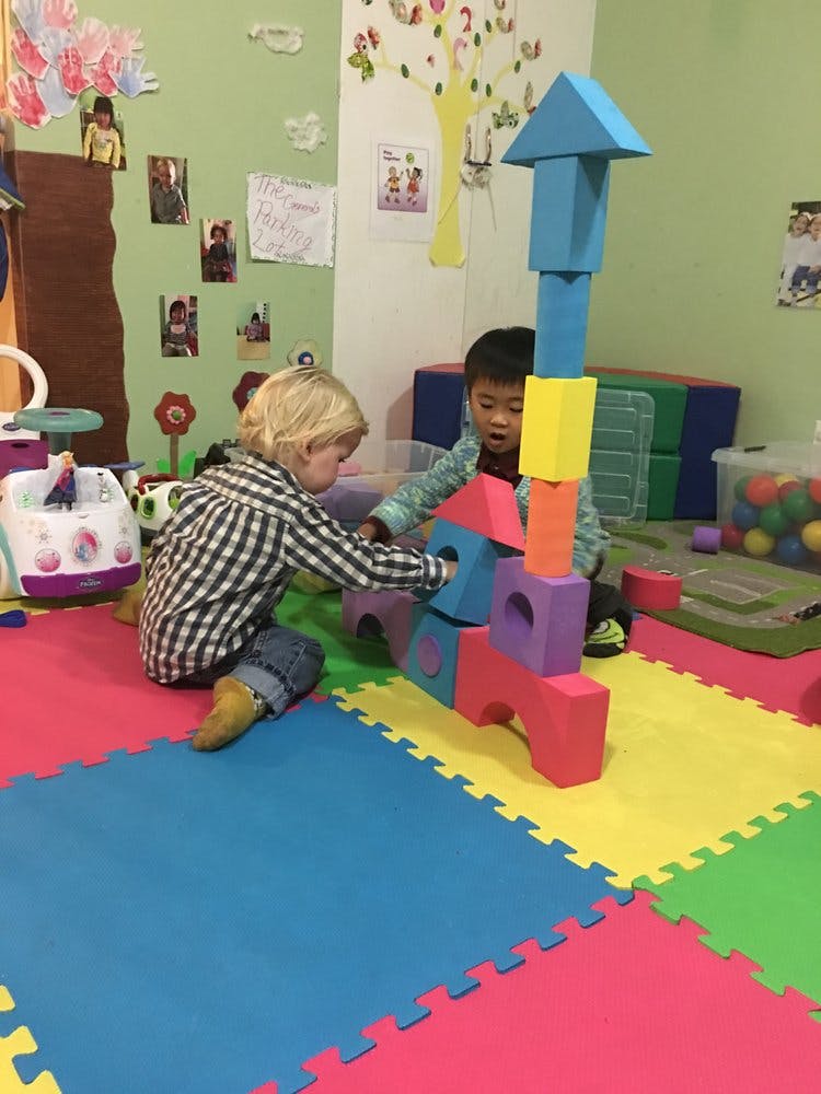 Two children playing with colorful building blocks on a padded floor