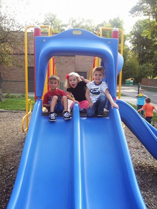 Three children sitting at the top of a blue playground slide