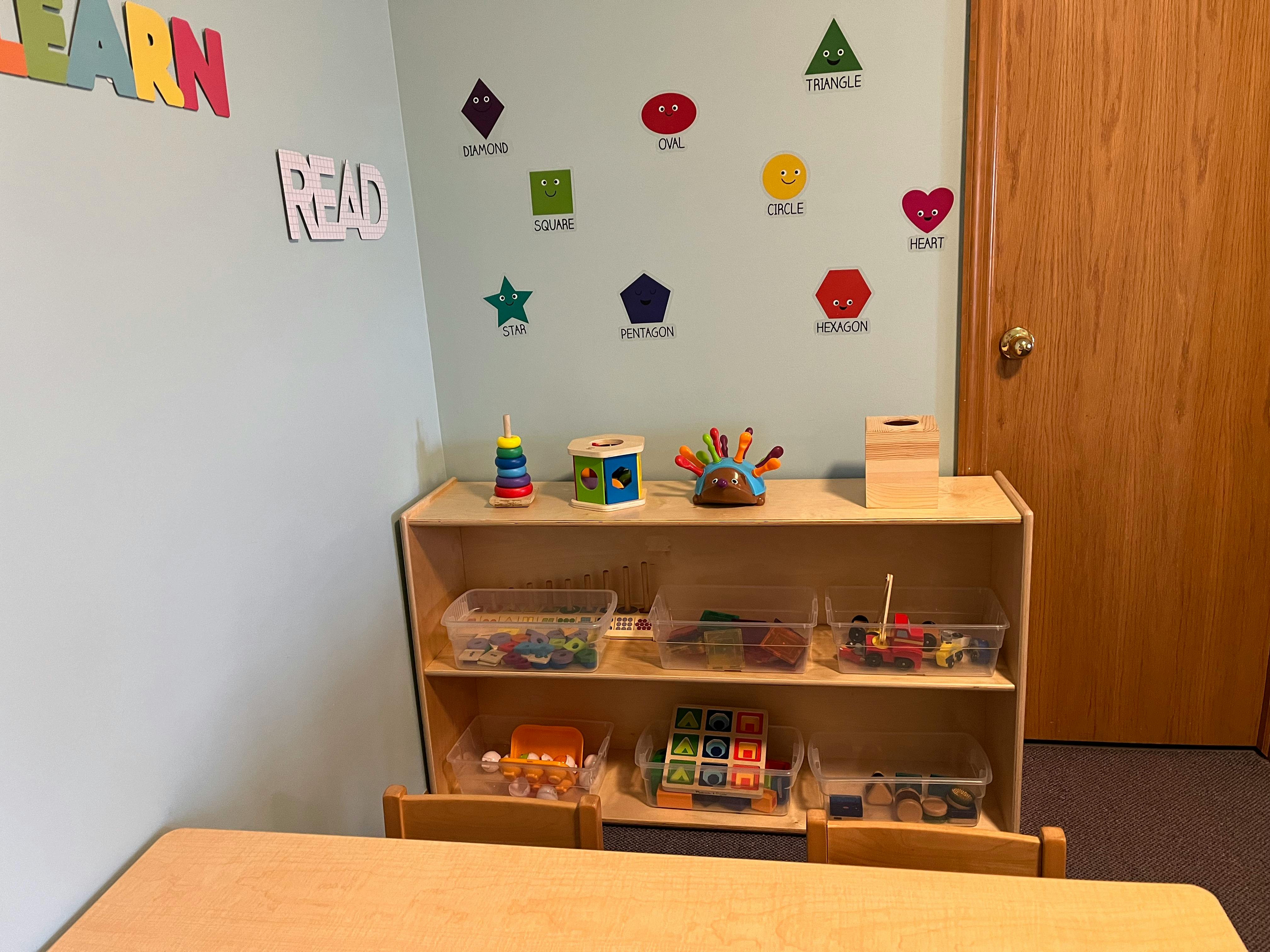 Classroom with a wooden shelf holding toys and clear bins