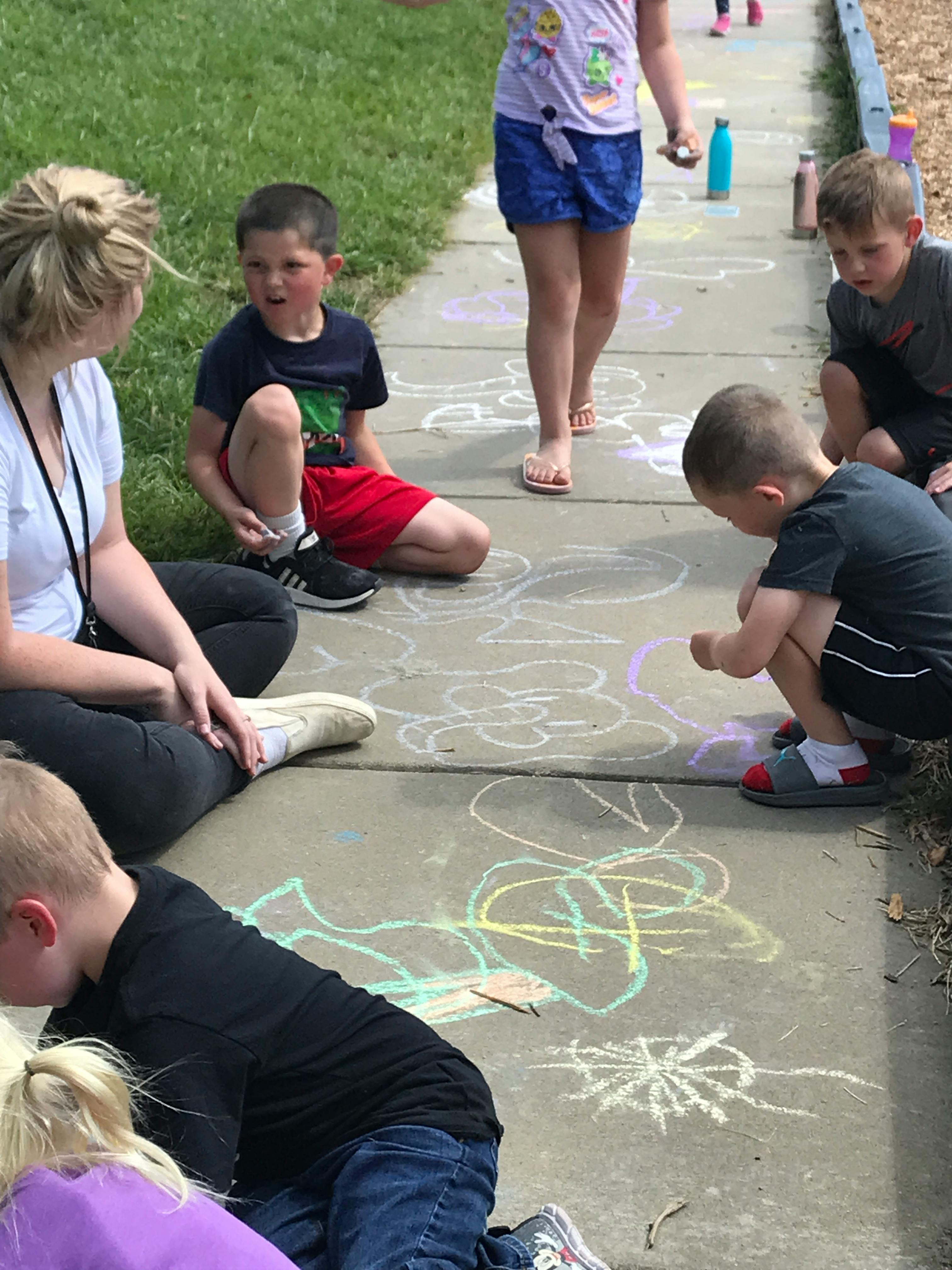 Person and children drawing with chalk on a sidewalk