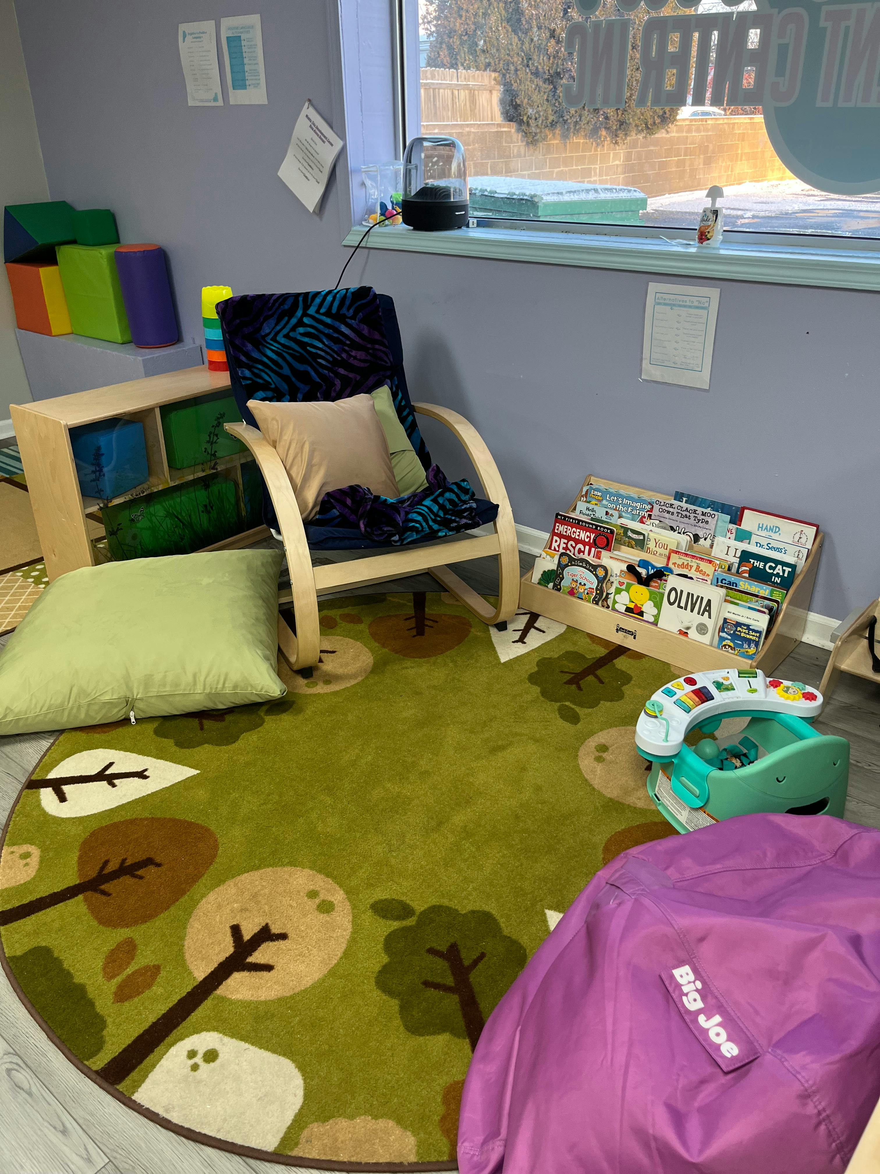 Child's play area with a green rug, rocking chair, and book display