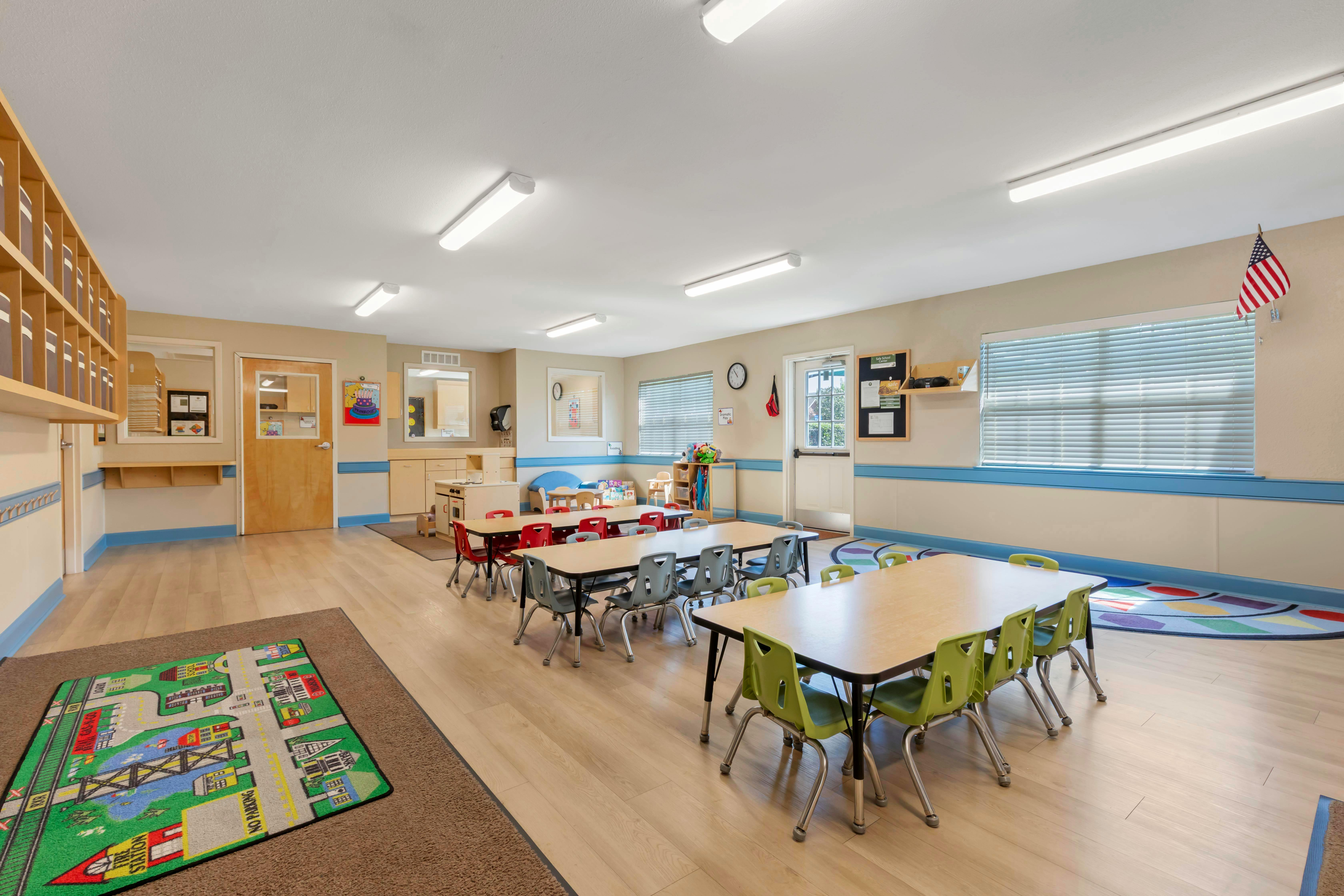 An empty childcare classroom with small tables and chairs