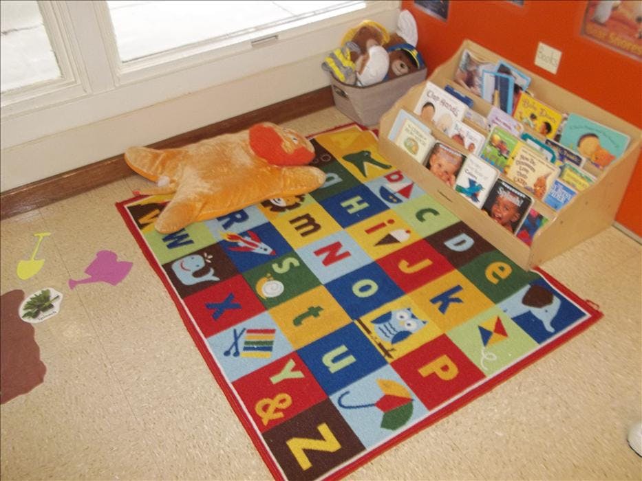 Classroom corner with alphabet rug, orange pillow, and book stand