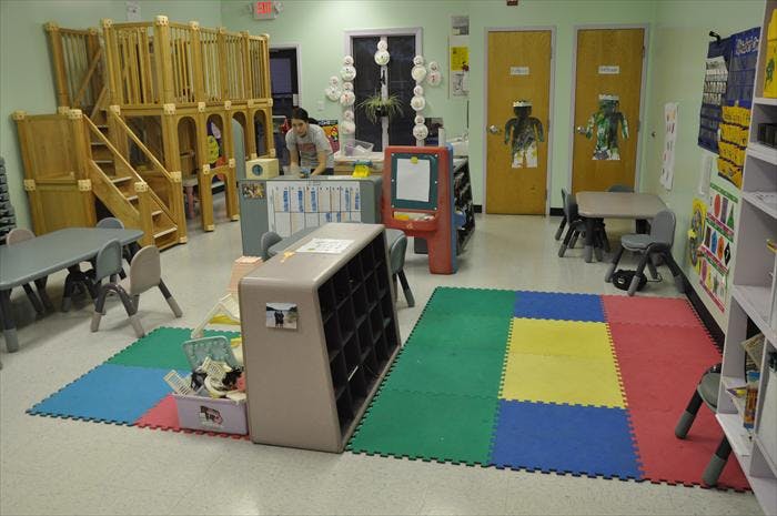Playroom with wooden play structure, tables, and colorful floor mats
