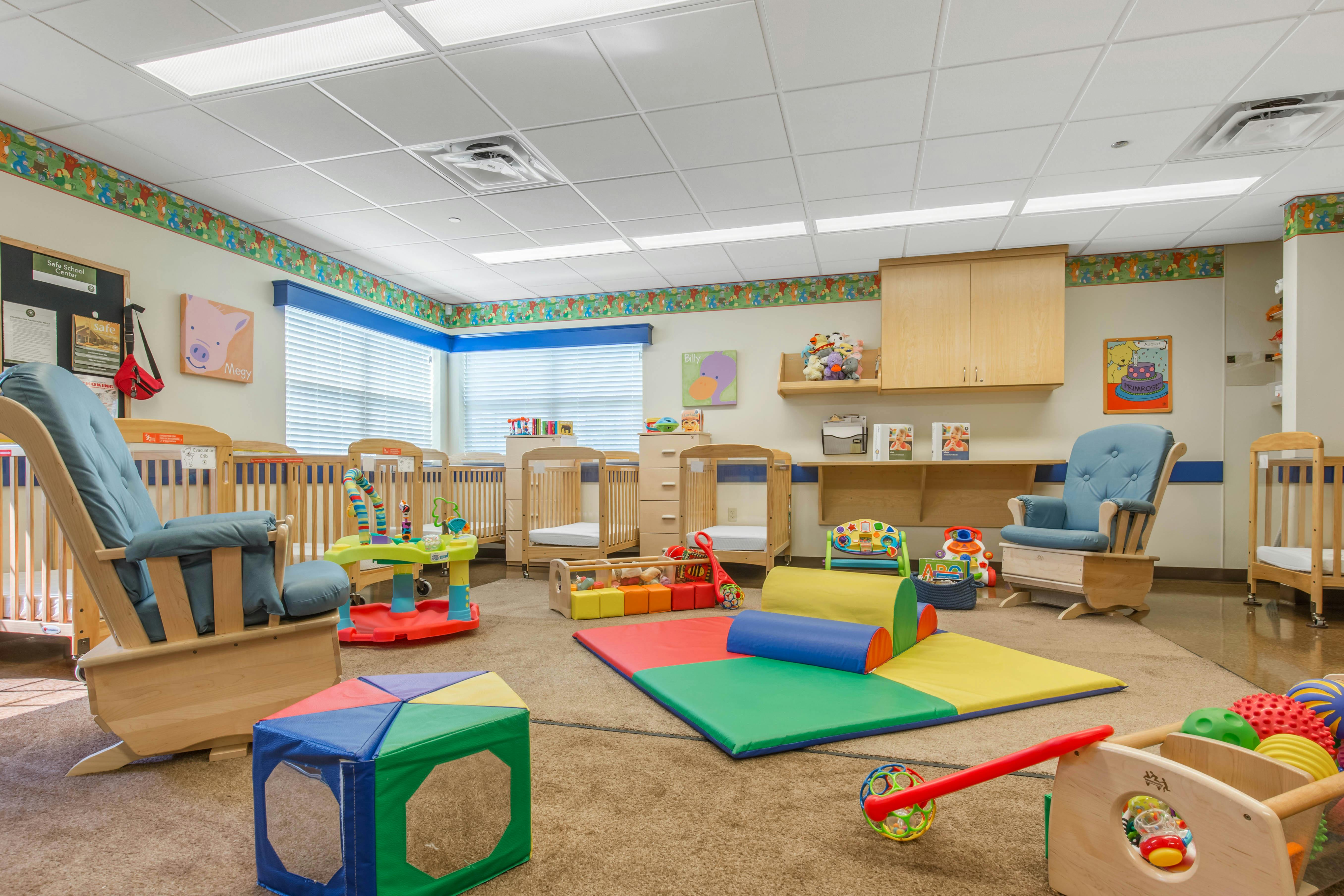 An empty nursery room with cribs, play mats, rocking chairs, and toys