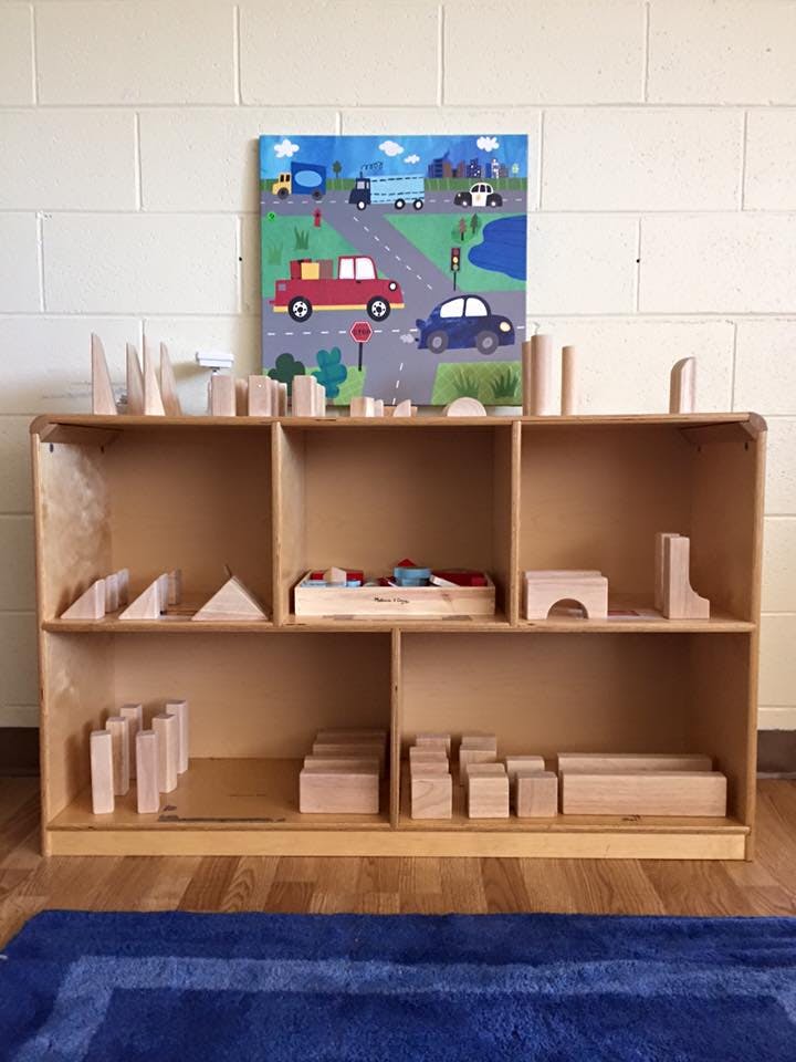 Wooden shelving unit with various wooden blocks and a car-themed painting above