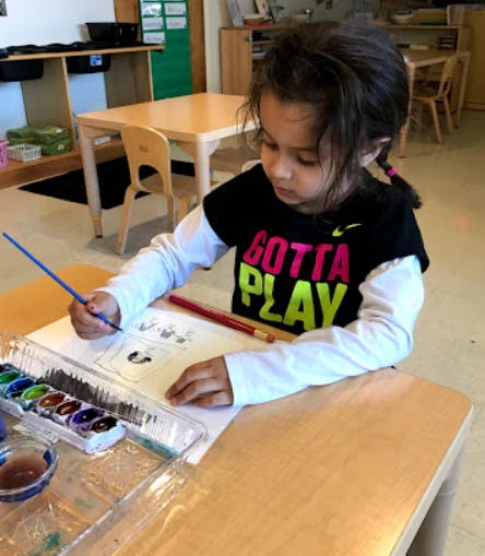 Child painting at a table in a classroom