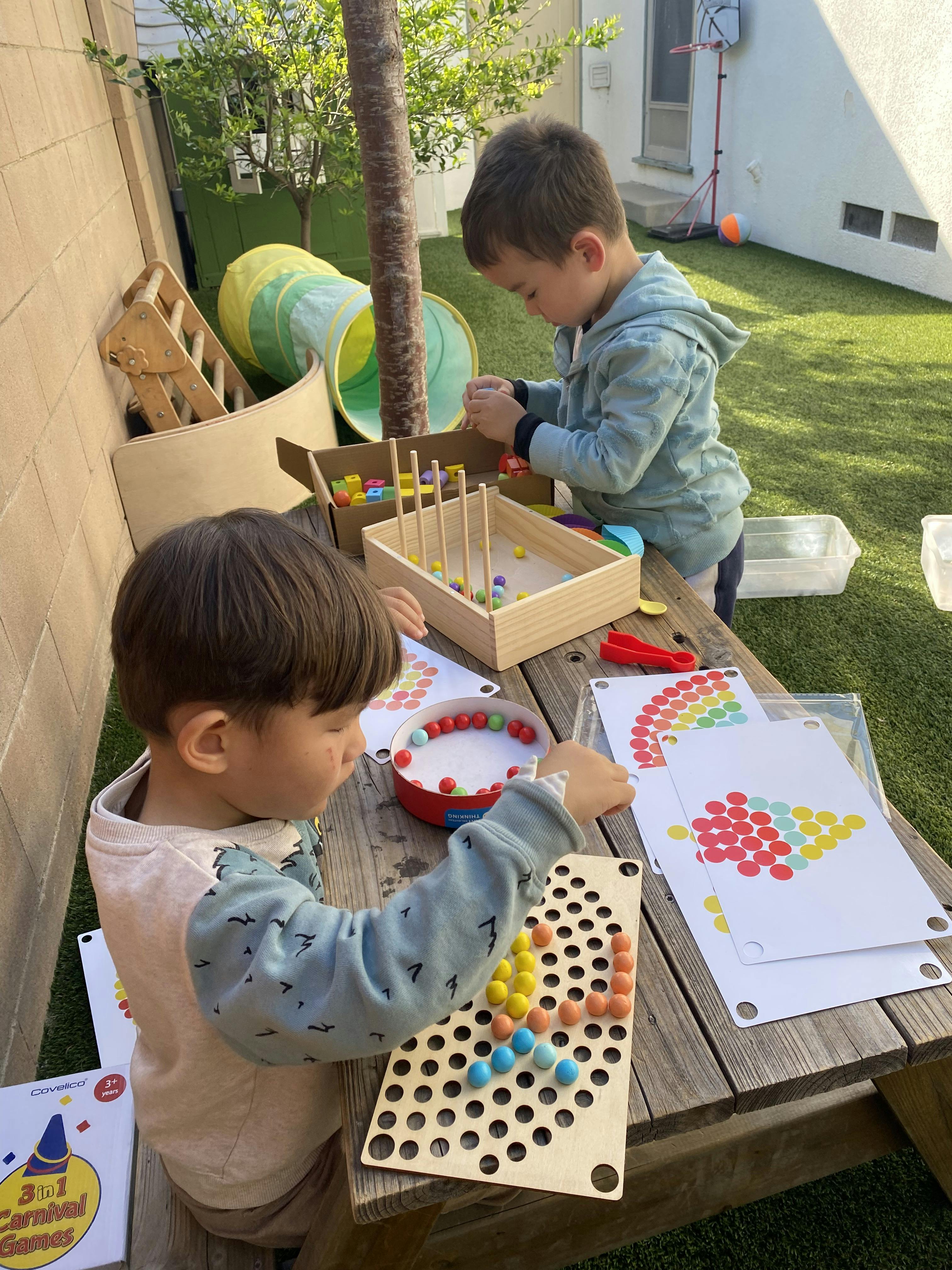 Two children playing with colorful sorting games on a wooden table outdoors