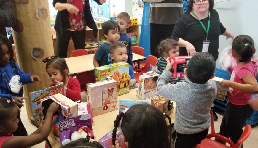 Children and adults in a classroom opening gifts