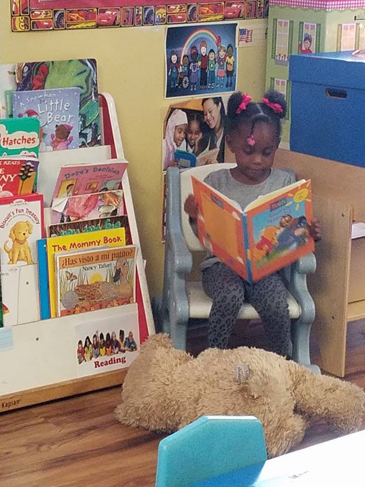 Child sitting in a chair reading a book in a classroom