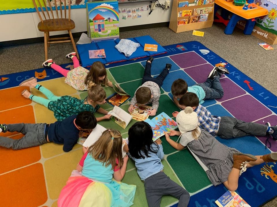 Children lying on a colorful rug reading books in a classroom