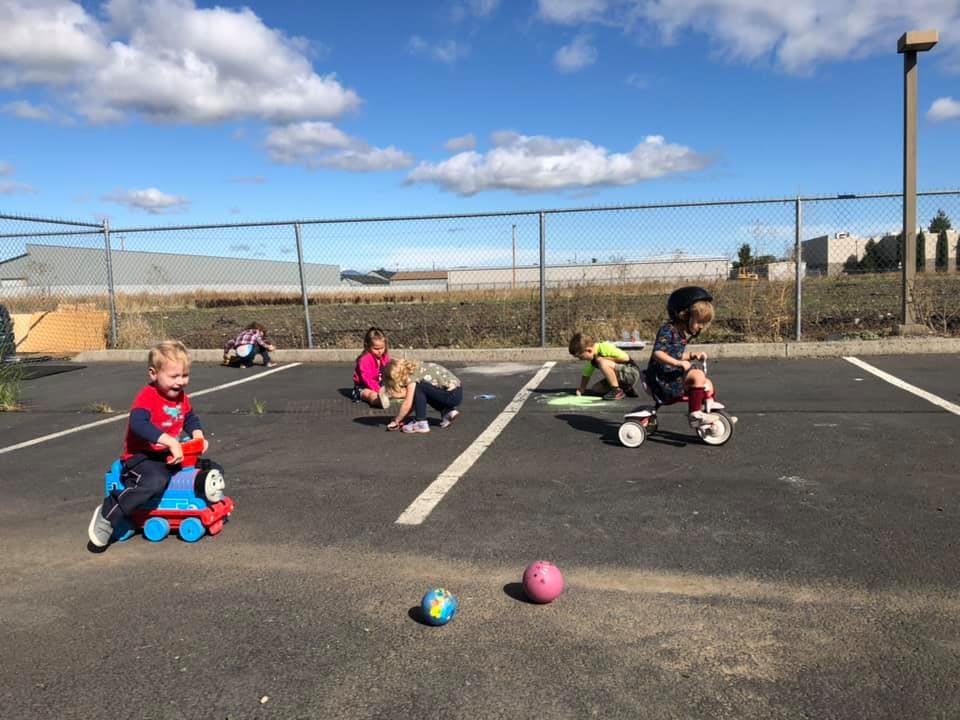 Children playing with ride-on toys and balls in a paved area