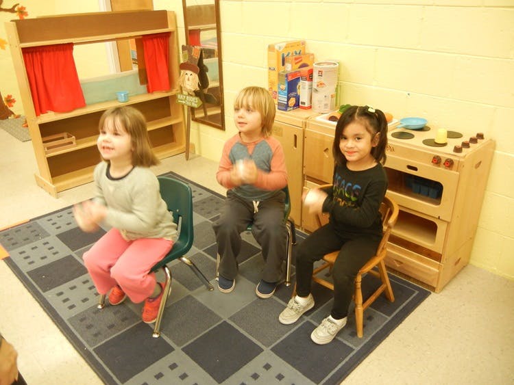 Three children sitting on chairs in a classroom