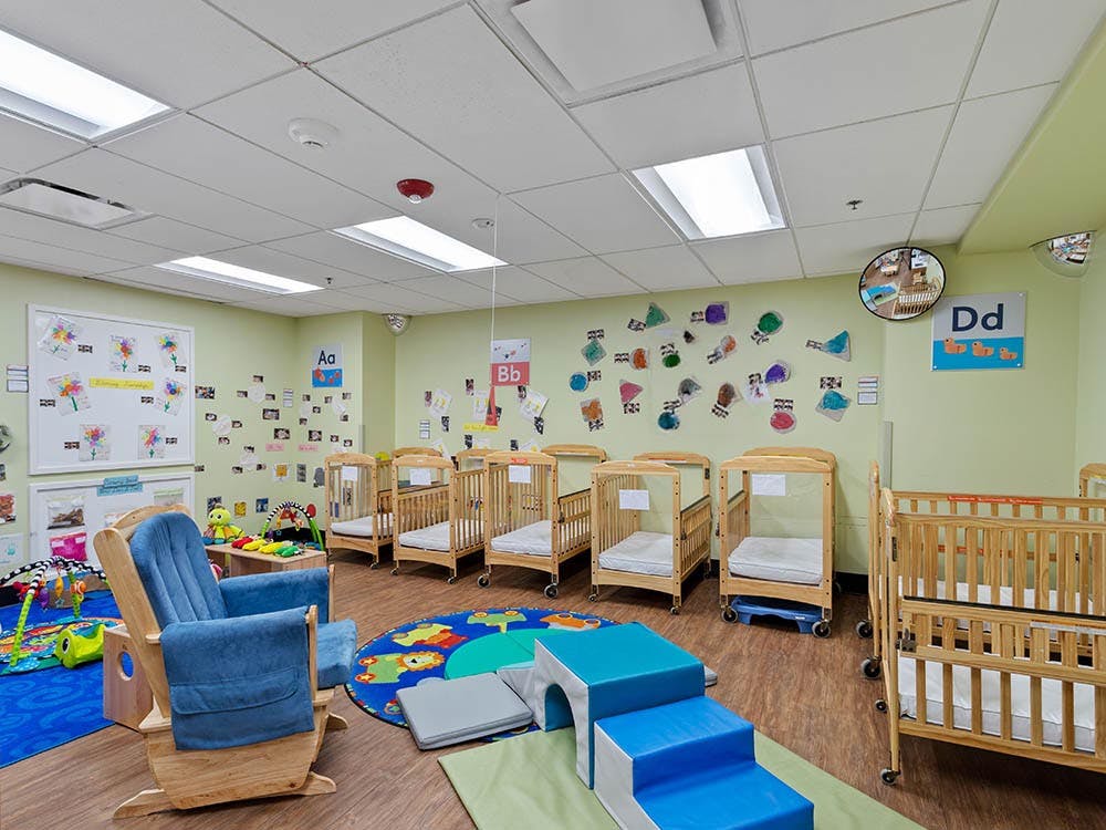 Baby room with several cribs, a rocking chair, and play mats on the floor