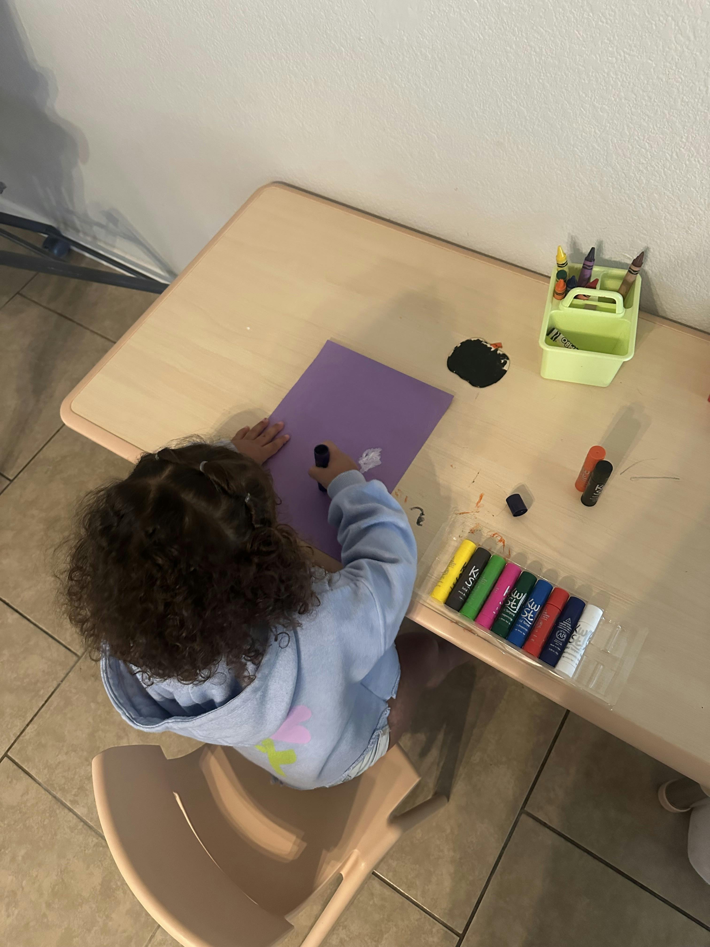 Child drawing with paint sticks on purple paper at a table