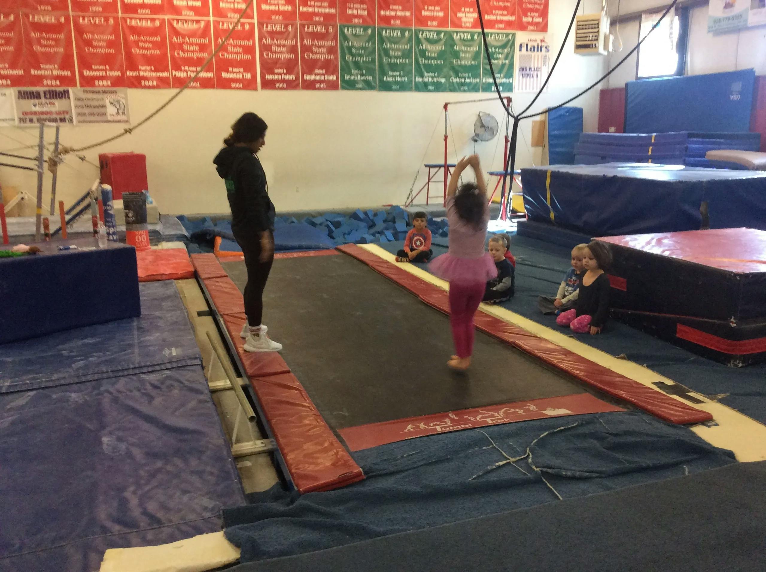 Person standing on a balance beam next to a child on a trampoline