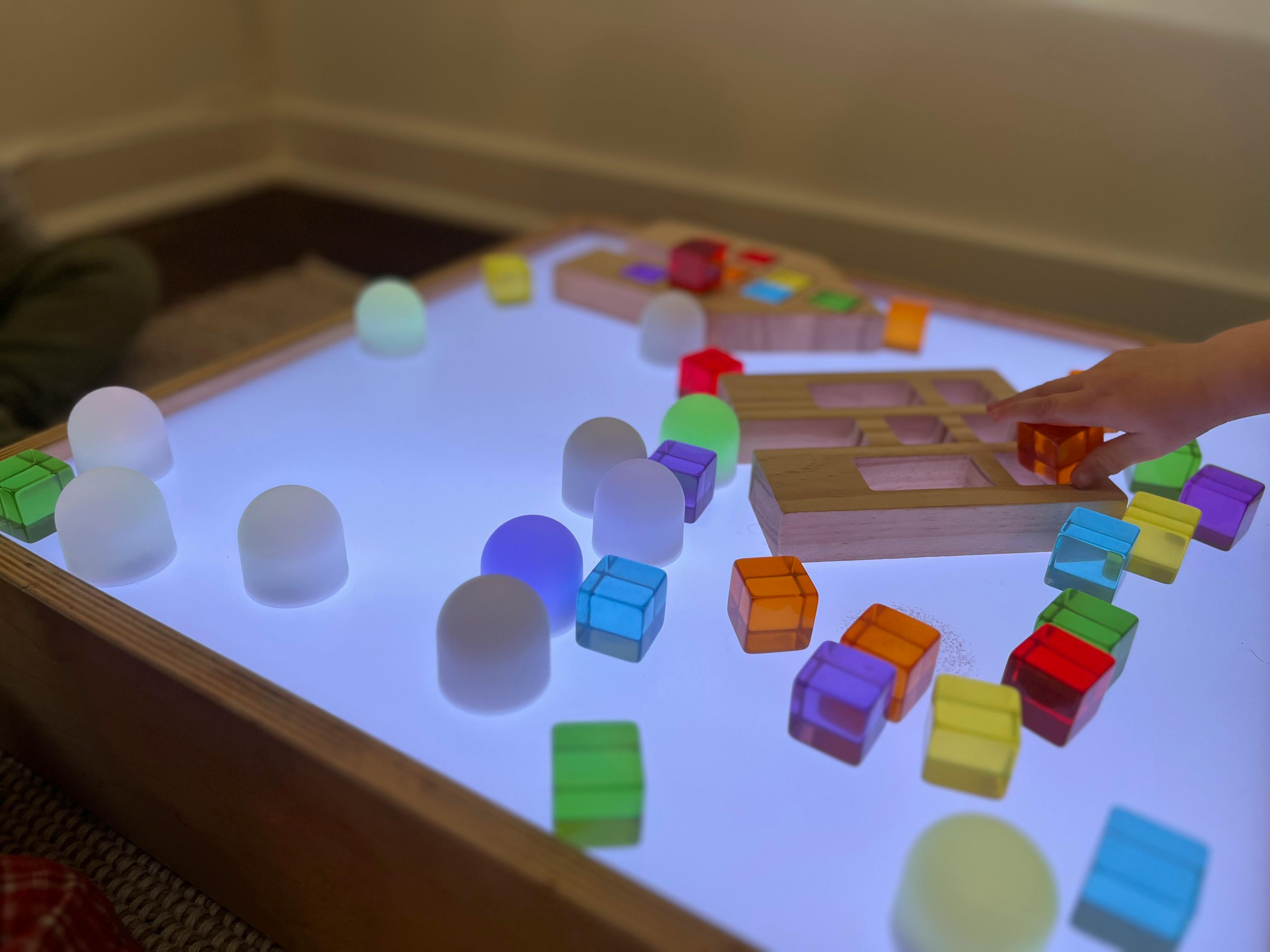 Child's hand playing with colorful blocks on a light table
