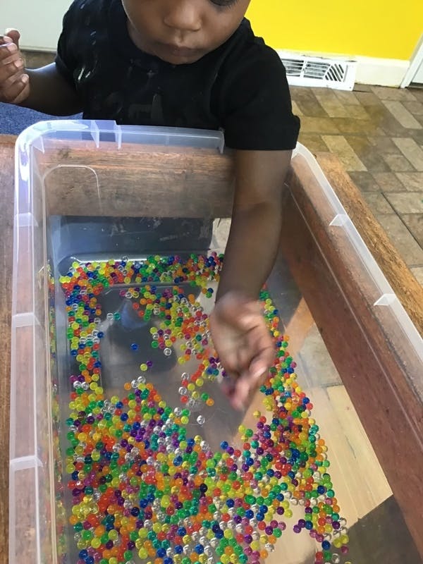 Child playing with colorful water beads in a clear container