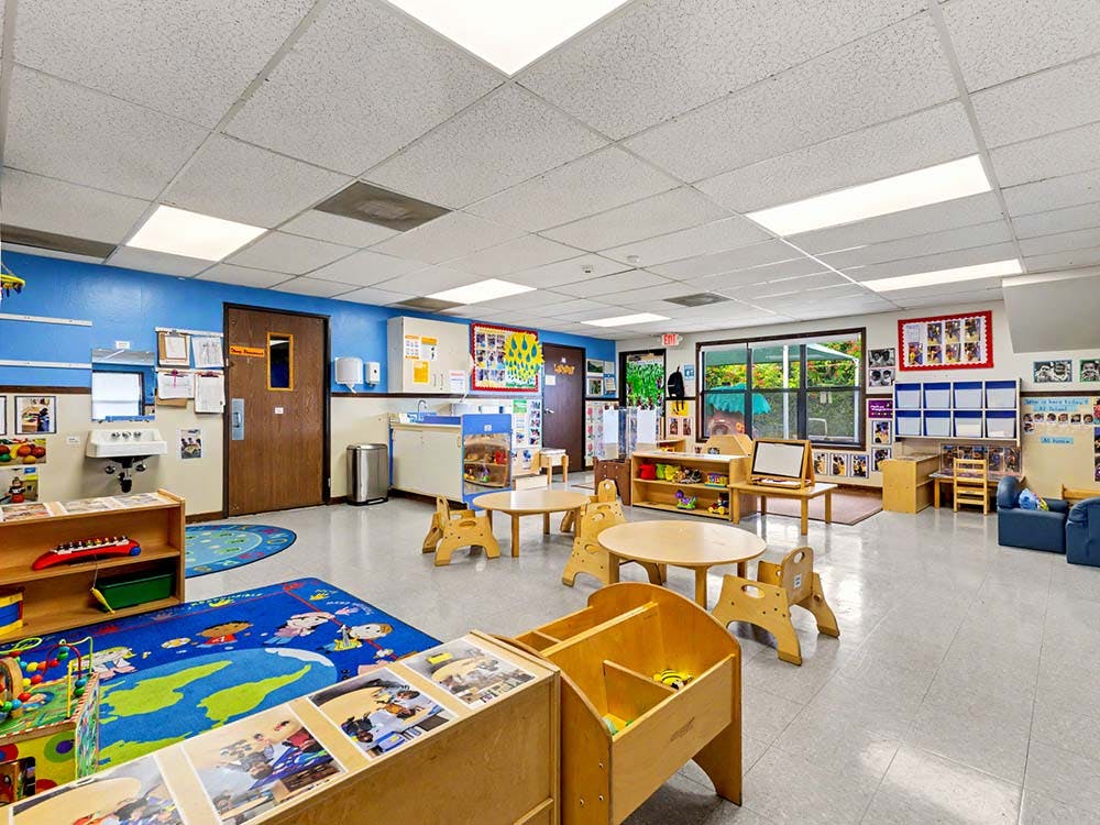 Empty classroom with small tables, chairs, and play areas