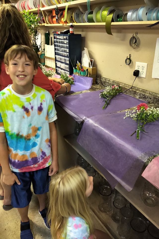 Child smiling while another person arranges flowers on a counter