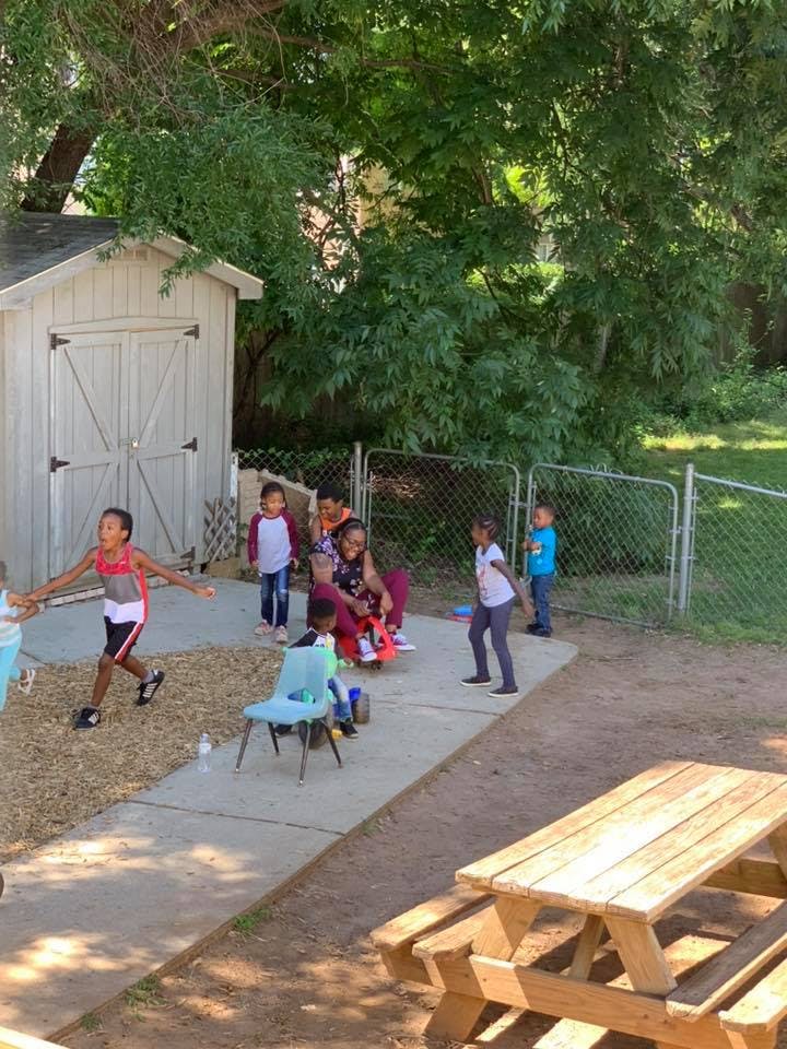 Children and adults playing outdoors near a shed and fence