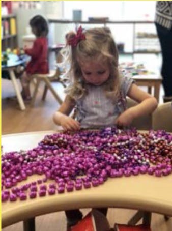 Child playing with many small purple objects on a table