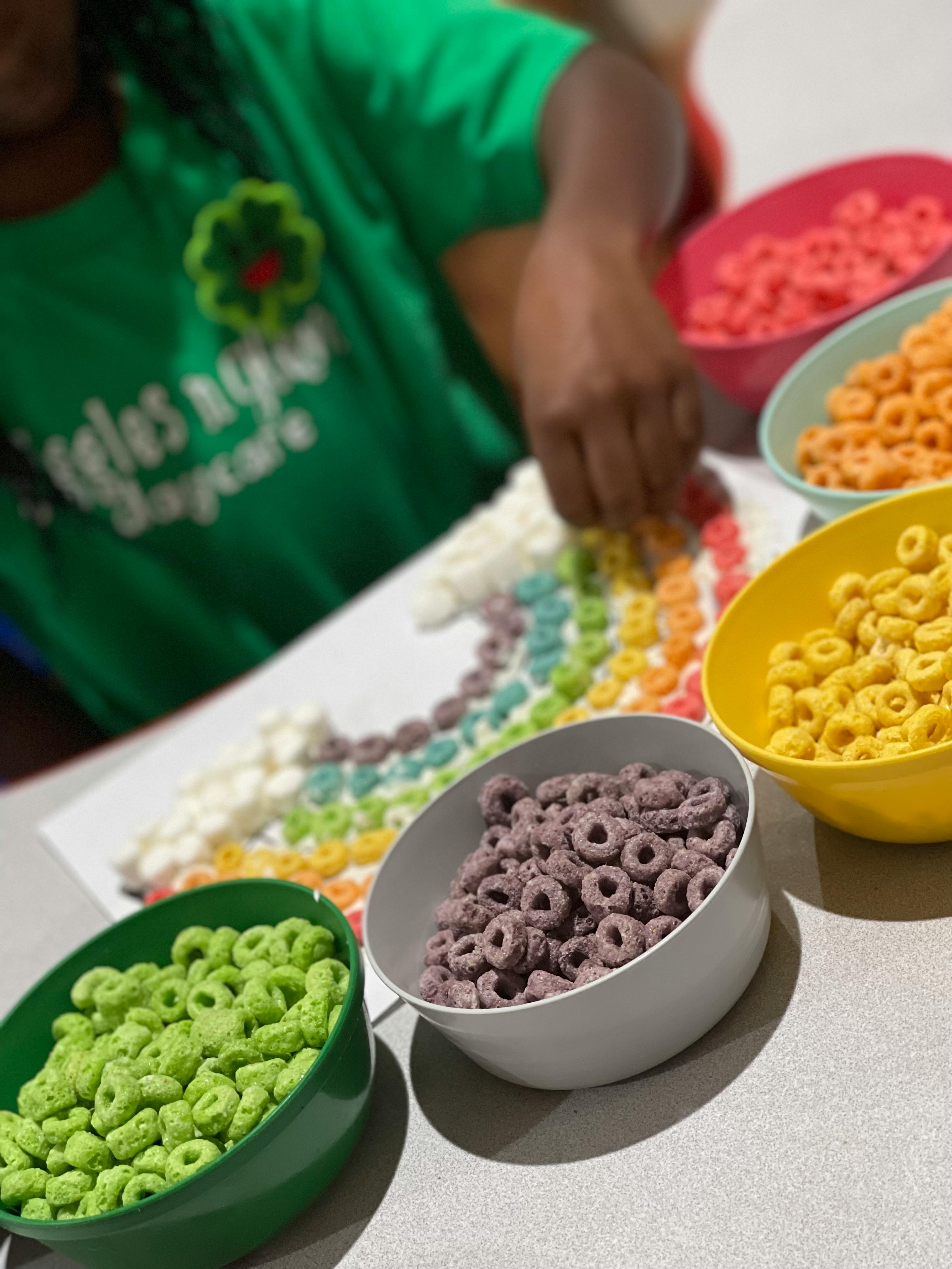 Person making a rainbow design with colorful cereal pieces