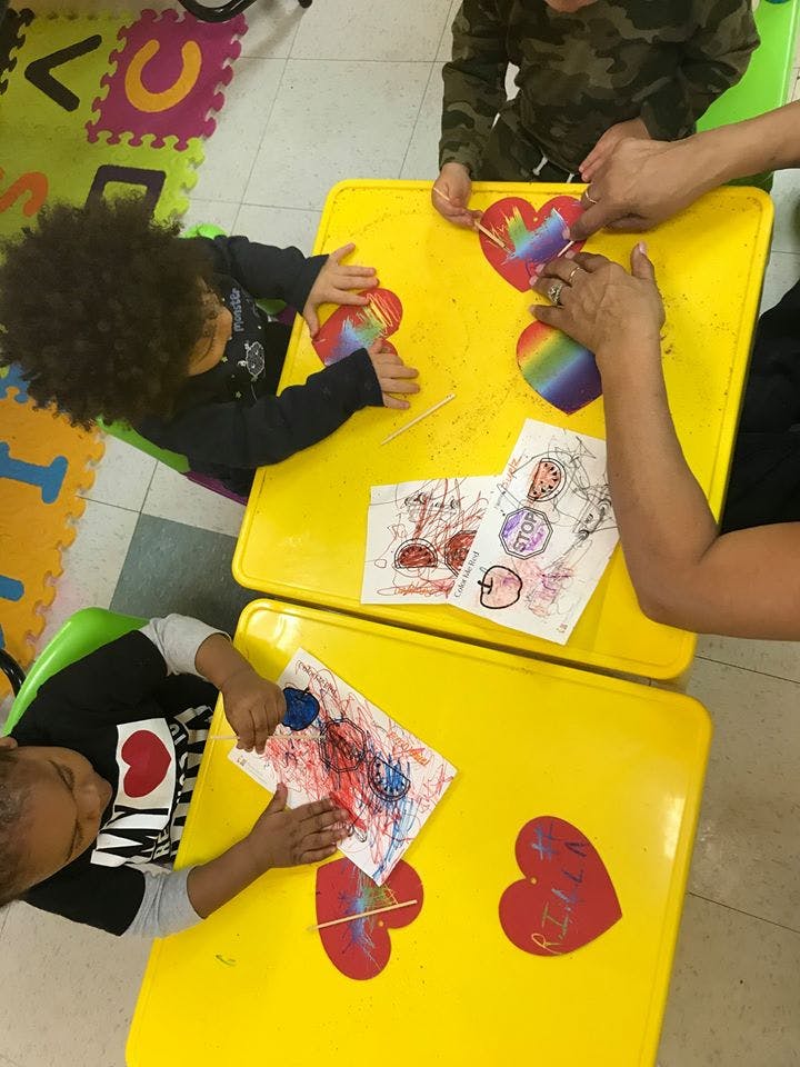 Children and an adult doing crafts at yellow tables in a classroom