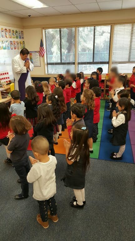 Adult and children standing with hands together in a classroom