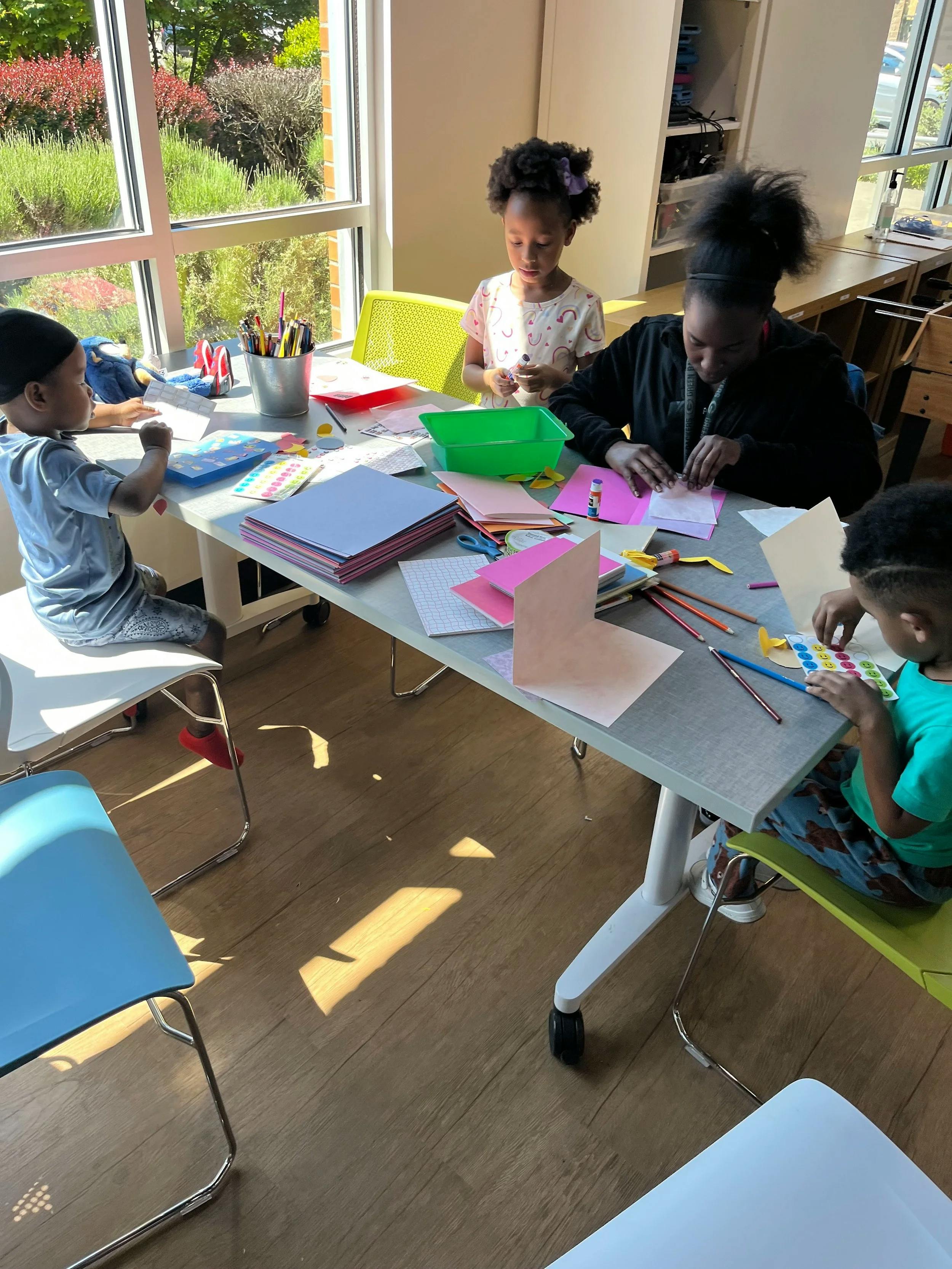 People creating art at a table with papers, stickers, and art supplies