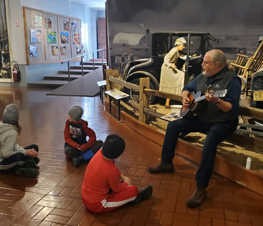 Person playing guitar for three children sitting on the floor