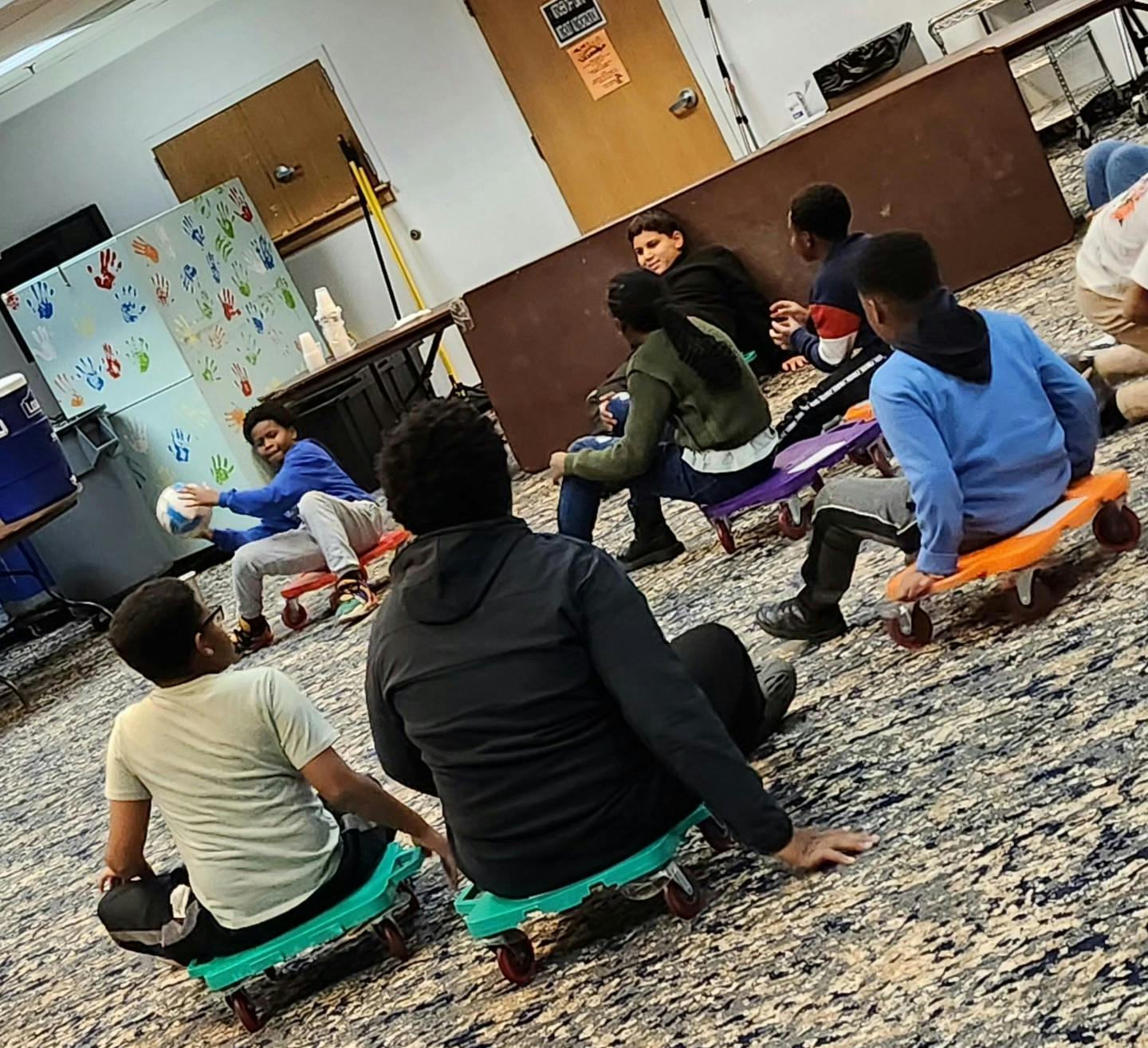 Teens sitting on scooter boards on a carpeted floor