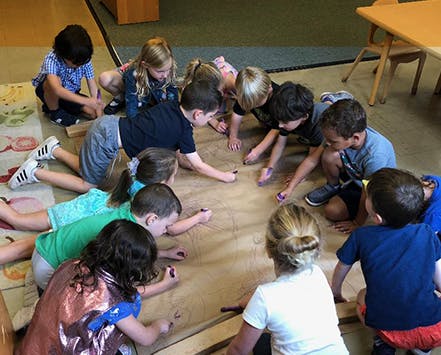 Children drawing on a large piece of paper on the floor