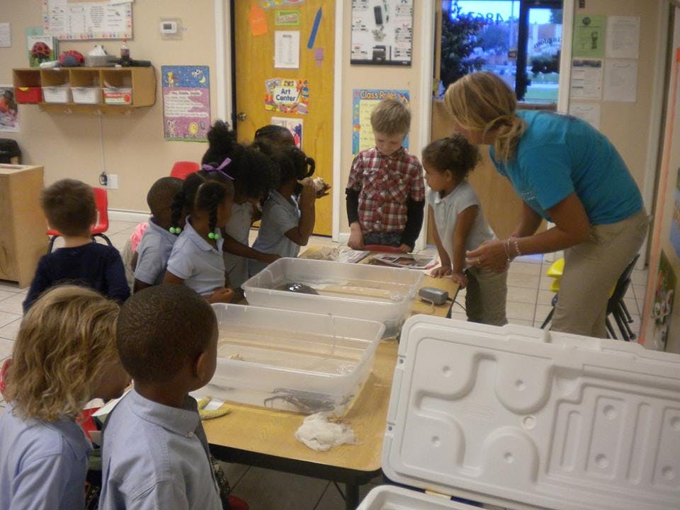 Adult and children gathered around a table with clear bins in a classroom