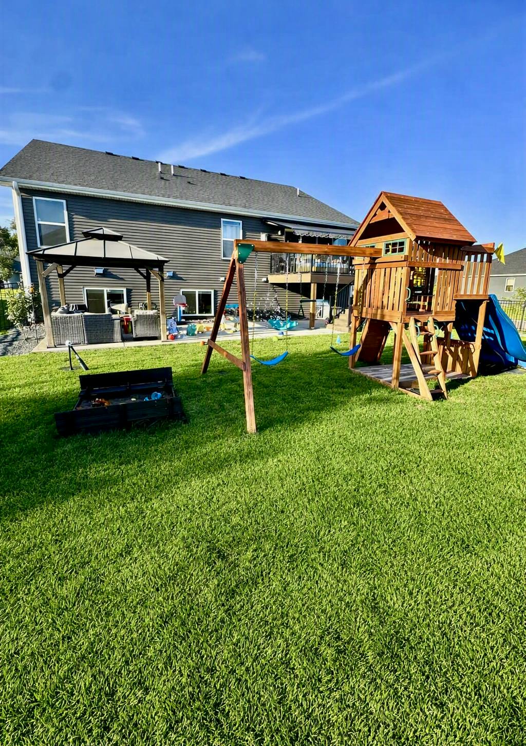 Wooden playset with swings and slide in a backyard with a gazebo